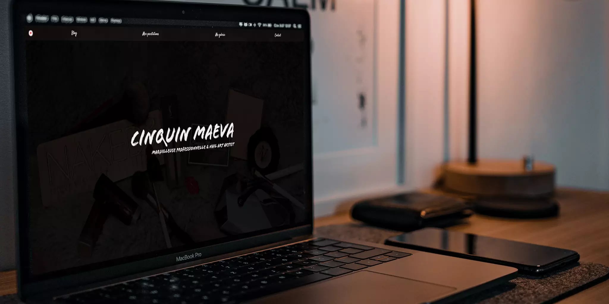 Modern workspace with a laptop displaying a portfolio website, accompanied by a mobile phone and a floor lamp in the background.